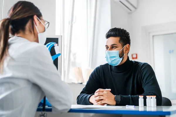 Portrait of an Indian male patient in a doctor\'s consultation, the doctor holds out his hand with an ampoule for vaccination.