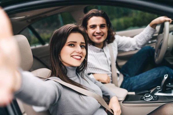 Happy young couple in the car, enjoying the trip, taking a selfie for memory, good impressions of a modern car.