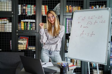Gülümseyen bir sarışının fotoğrafı, üniversite öğrencisi, üniversite öğretmeni, online dersler. Kütüphanede güzel bir öğrenci gülümseyerek kameraya bakar..