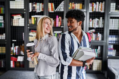 Çok uluslu, Hintli öğrenci Avrupalı öğrenci kıza bakar ve birbirine gülümser. Kütüphanedeler..