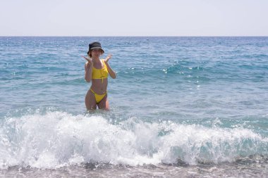 Yaz tatili tarzı, kumsalda yürüyen sarı bikinili, ince, kızıl saçlı güzel bir kız. Türkiye 'de mavi kristal berrak denizde mutlu gezgin kadınlar, Kemer.