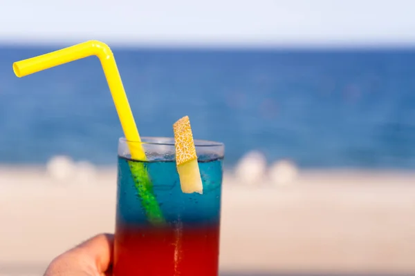 暖かい青い海を背景に カラフルな青と赤の層状のトロピカルアルコールカクテル 異国情緒あふれる夏休み — ストック写真