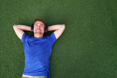 Müzik dinlerken çimenlerde uzanan, güneş gözlüğü takan gülümseyen bir adamın portresini yakından çek. İki eli çimlerin üzerinde uzanmış, mutlu bir adam.                          