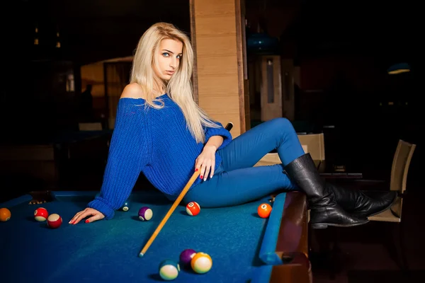 Sexual blonde lady posing on billiard table with the cue