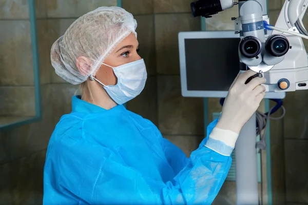 Médico en mascarilla respiratoria cheks microscopio quirúrgico en la operación r —  Fotos de Stock