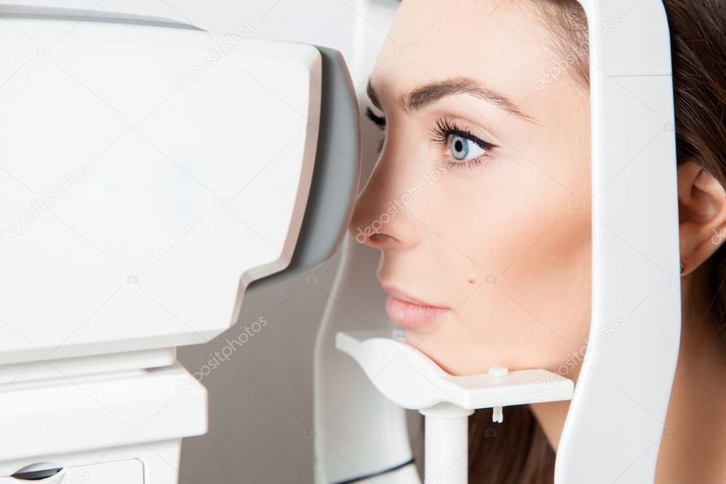 Sweet young adult brunette looking at eye test machine in ophtha