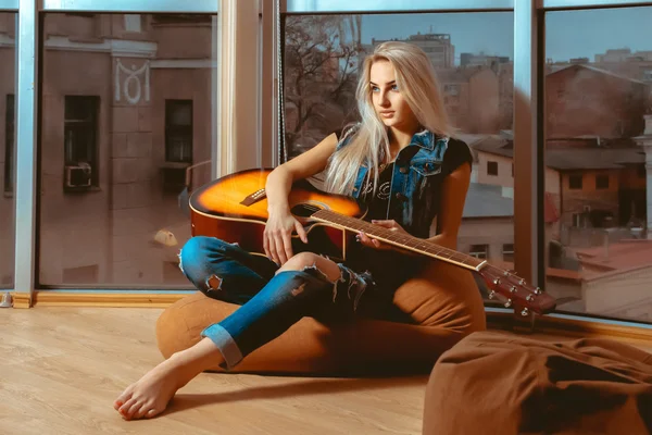 Mädchen, das mit einer Gitarre in der Hand in der Nähe der großen Fenster liegt. — Stockfoto