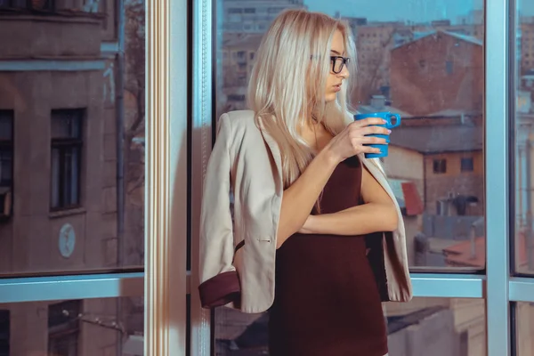 Portret van jonge blonde zakenvrouw met kopje thee in de buurt van de — Stockfoto