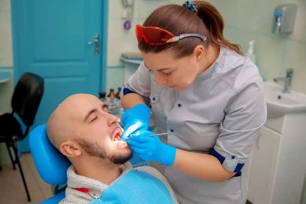 Handsome guy in dental office treats teeth — Stock Photo, Image