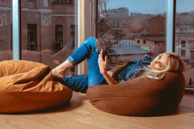 İnce genç sarışın koltukta yalan ve cep telefonunu yazarak