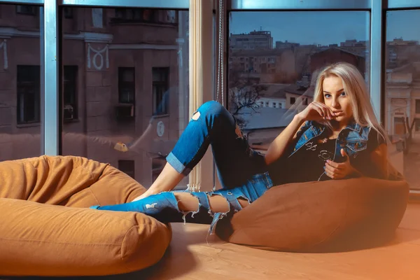 Cute young blonde woman posing on orange couch near the large wi — Stock Photo, Image