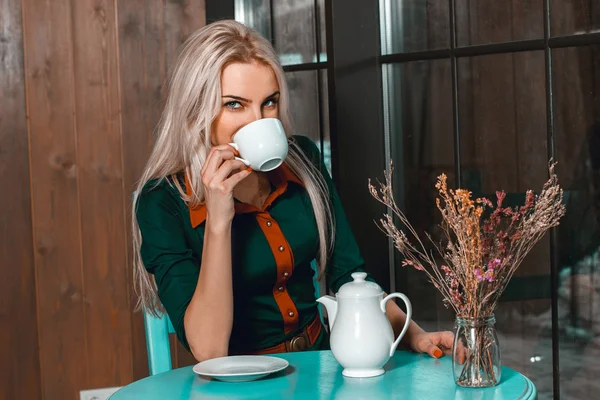 若い美しいブロンドの女の子は、カフェと c を見て茶を飲む — ストック写真