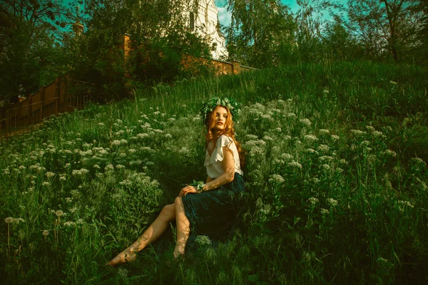 Kobieta siedzi na trawie z wieniec na głowę — Zdjęcie stockowe