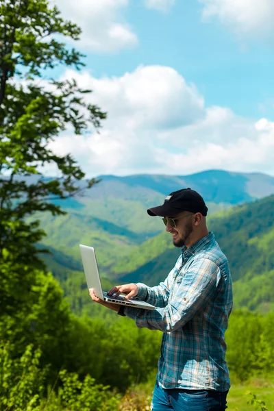 dağlarda dizüstü bilgisayarda çalışan genç adam