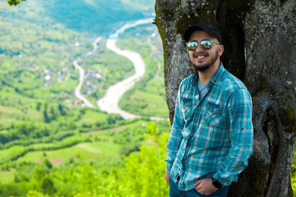 男は笑みを浮かべて、b からの山の風景と木の近くのポーズ — ストック写真