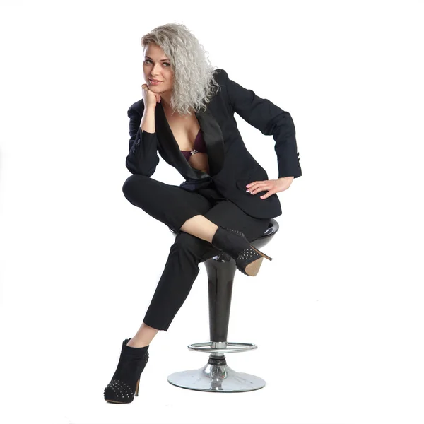 Vrouw met blond krullend haar in zwart pak zit op chai — Stockfoto