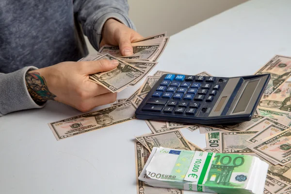 masadaki adam hesap makinesi üzerinde bir sürü para düşünüyor.