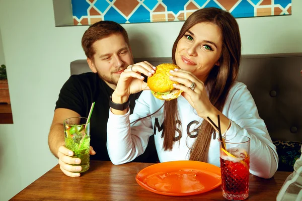 Casal posando no café com hambúrguer e coquetéis — Fotografia de Stock
