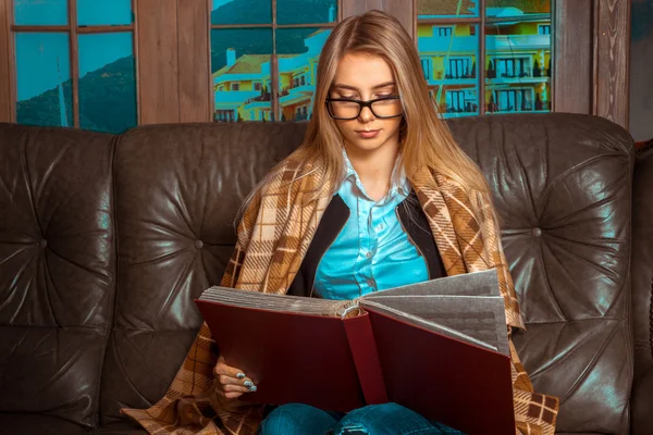 Bella ragazza su un divano di pelle con un libro in mano — Foto Stock