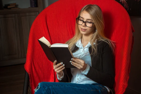 Mooi meisje het lezen van een boek in een leunstoel — Stockfoto
