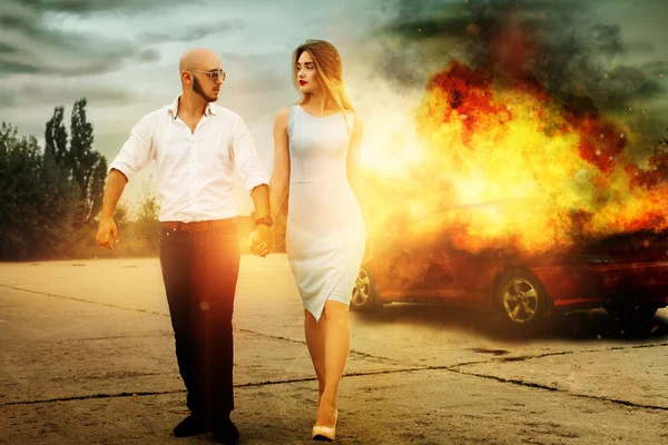 Man and a woman go away from burning car — Stock Photo, Image