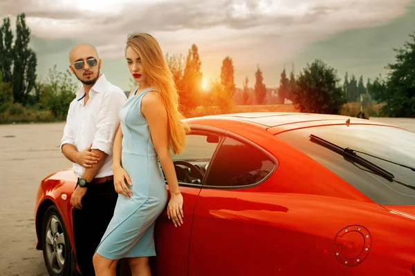 Girl with man posing at sunset with sport car — Stock Photo, Image