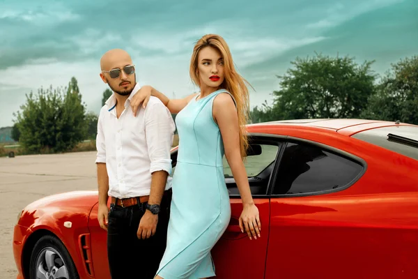 Preciosa mujer y hombre guapo con coche deportivo rojo — Foto de Stock