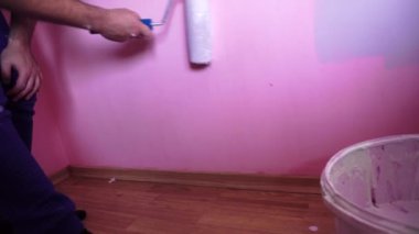 Adam odanın duvarlarını boya rulosuyla boyuyor.