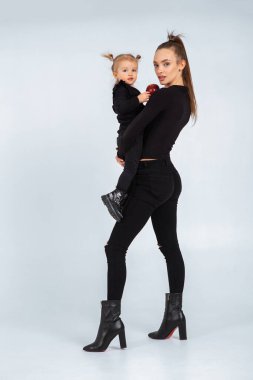 Siyah elbiseli seksi genç anne küçük kızını stüdyoda elinde tutuyor.