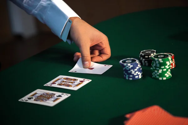 Närbild av en mans hand öppnar korten vid ett pokerbord med en — Stockfoto