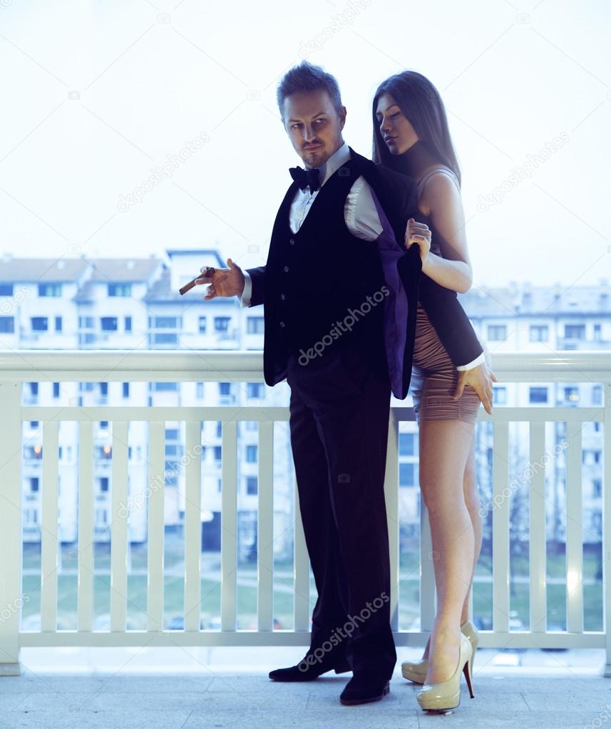 Trendy csexy couple posing on balkony in stylish suits