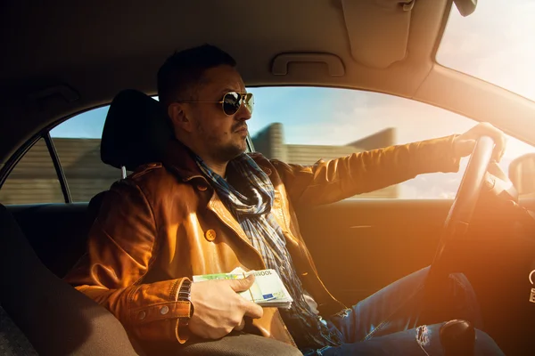 Stylish male model holding a lor of money EUR and driving car — Stock Photo, Image