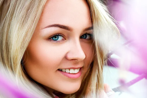 Schönheit junge Blondine lächelt neben rosa blühenden Blumen — Stockfoto