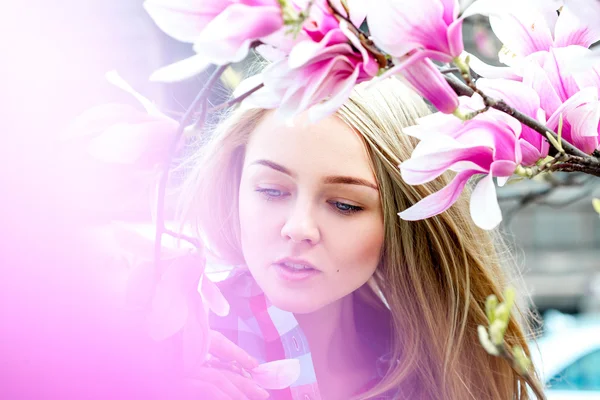 Gorgeous young blonde woman with blue eyes posing near blooming — Stock Photo, Image