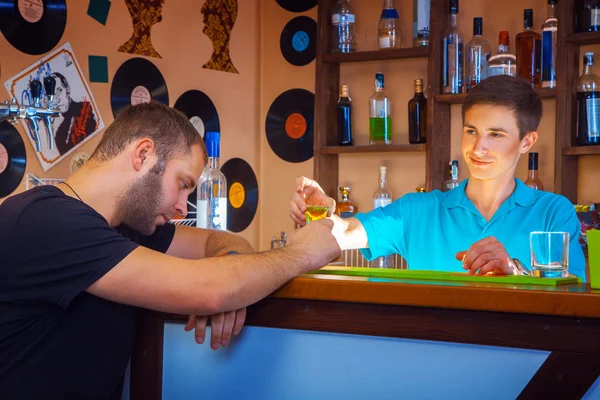 barman gives short cocktail to drunk unshaved man at bar table