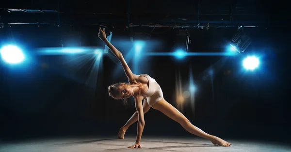 Ballerina posing on stage against spotlights — Stockfoto