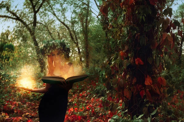 Fantástica jovem bruxa evoca por um livro mágico na floresta — Fotografia de Stock