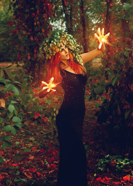 Fantastic young witch conjures in the forest outdoors
