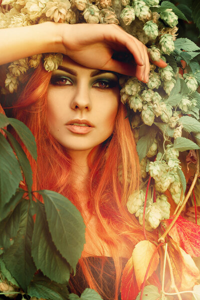 Fresh portriat of sexy redhair lady in leaves with wreath of hop on head outdoors