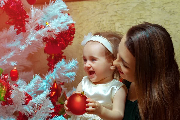 Maminka s malou dcerou zdobí vánoční strom a s — Stock fotografie