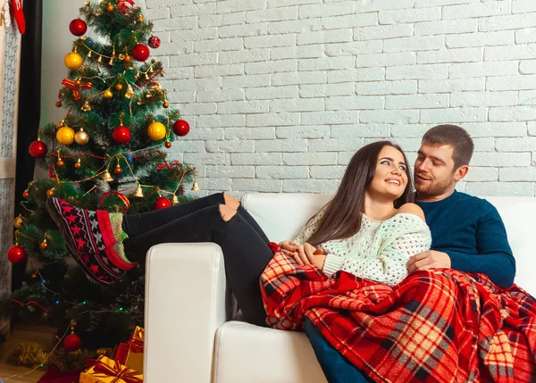 Nice couple in love lies on a couch wrapped in plaid Christmas E — Stockfoto