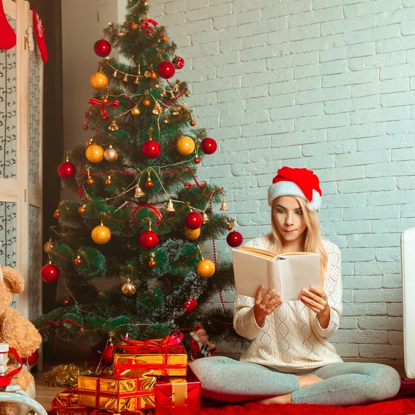 Bedårande blondin läser saga på julafton i santa hatt — Stockfoto