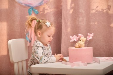 Doğum gününde pijamalı küçük bir kız çocuk masasında beyaz bir sandalyede oturuyor.