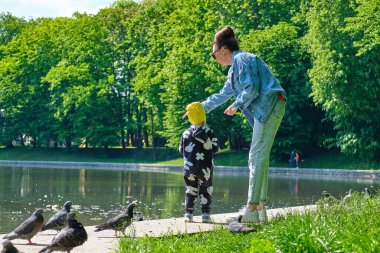 Anne ve kızı şehir göletindeki güvercinlere ekmek kırıntıları yediriyorlar.