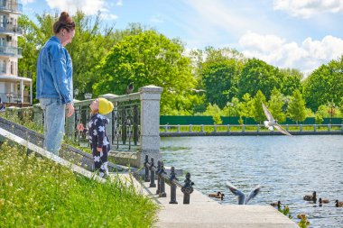 Anne ve kızı, şehrin göletindeki ördek ve martılara ekmek kırıntıları yediriyor.