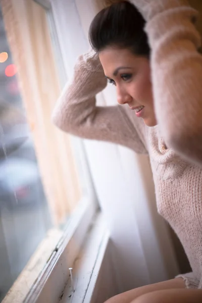 Mujer bonita en suéter mirando por la ventana — Foto de Stock