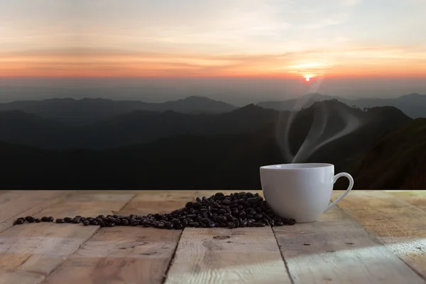 Tasse schwarzen Kaffee und Bohnen über Holztisch und Sonnenuntergang Stockbild