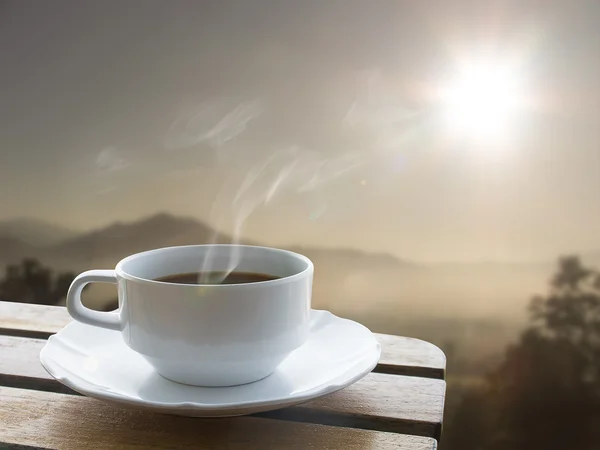 Kopp kaffe och över bord av trä och soluppgång bakom berget Stockbild