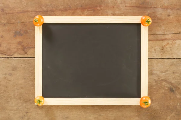 Blackboard en tomaat op houten achtergrond — Stockfoto