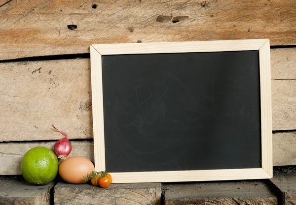 Blackboard and ingredients on wooden background — Stock Photo, Image